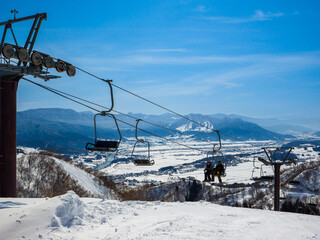 A scenic view of a snowy valley and distant ski resort looking through chairlifts on a sunny winter day (Togari Onsen, Nagano, Japan)