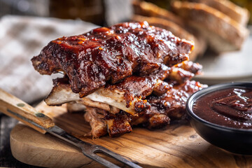 Pork BBQ glazed ribs and sauce on wooden cutting board.