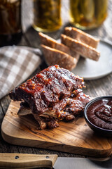 Pork BBQ glazed ribs and sauce on wooden cutting board.
