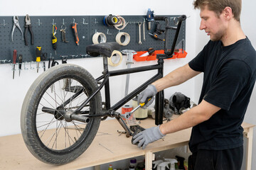 Fototapeta premium A person in gloves is tightening a bicycle crank on a bike frame using a ratchet wrench in a well-equipped workshop with tools in the background.