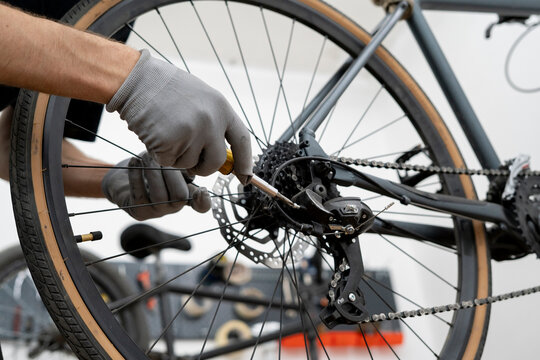A mechanic is making adjustments to a bicycle tensioner using a screwdriver in a well-lit workshop