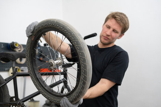 A mechanic is examining a BMX bike wheel closely in a workshop, ensuring it is properly maintained and ready for riding