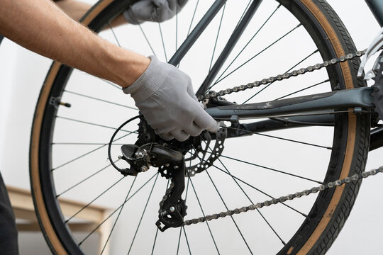 A bicycle mechanic repairs the rear wheel of a bike in a well-lit workshop, focusing on the brake system while wearing gloves for protection and cleanliness.