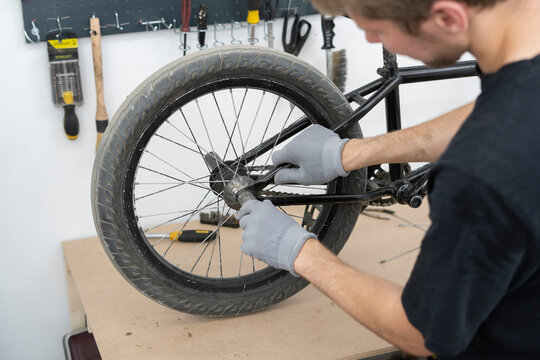 A cyclist is adjusting the seat of a BMX bike in a well-equipped workshop. Various tools and equipment are visible in the background, enhancing the repair process. - Powered by Adobe