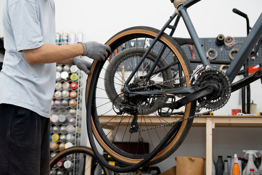 A person is repairing a bicycle by changing a flat tire, working diligently in a well-equipped workshop