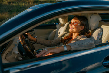 A joyful woman reveling in her stylish car while driving, experiencing happiness and freedom under the bright sun