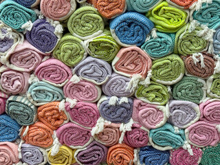 Rolled textiles with herringbone patterns in red, orange and gray stacked in a shop. Design, comfort and consumer choice represented through woven fabric, retail and cultural craft.
