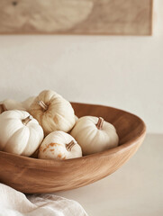 White mini pumpkins in a wooden bowl on beige background, minimal fall still life
