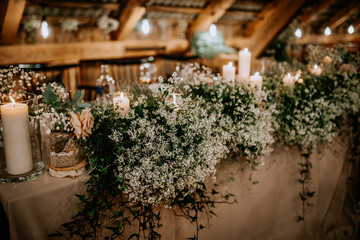 A beautifully decorated table with white candles, baby’s breath flowers, and rustic floral arrangements creates a romantic and elegant atmosphere for an event. © Raivo