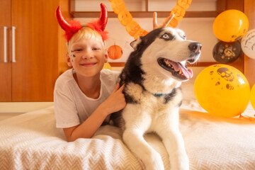 Happy child with a husky in Halloween costumes celebrates indoors The child laughs with costumes...