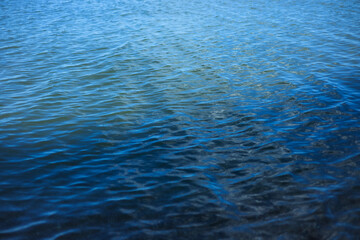Blue water with ripples on the surface. Defocus blurred transparent blue colored clear calm water surface texture with splashes and bubbles.