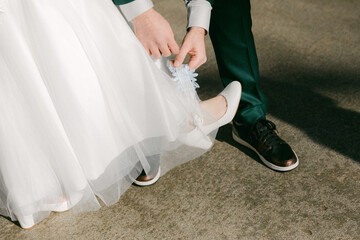 Groom adjusting bride's wedding dress during outdoor ceremony on sunny day in charming location