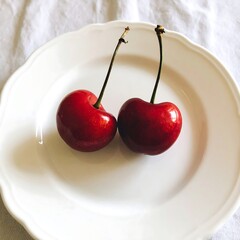 Two juicy cherries on a white plate