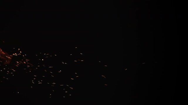 Slow motion vertical shot of fire and sparks and embers from campfire flying over black background