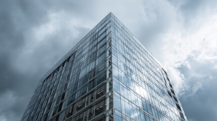 Fototapeta premium Modern glass building under dramatic cloudy sky reflecting sunlight during late afternoon