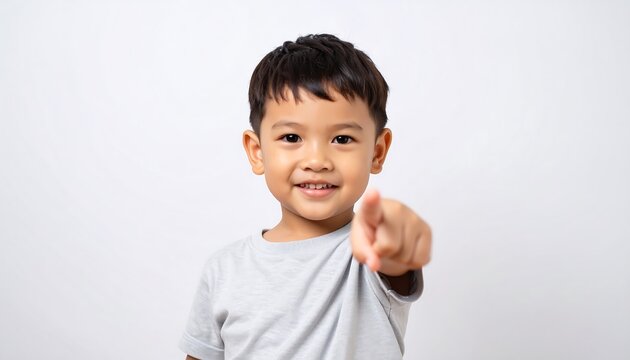 A cheerful little boy points directly at the camera, standing against a plain white background