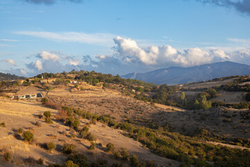 Rural hillside village with scattered houses and fields against mountain backdrop