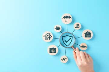Insurance Coverage Concept. Hand holding a magnifying glass over a shield icon surrounded by various types of insurance including health, life, travel, auto, home, and family, on a blue background.
