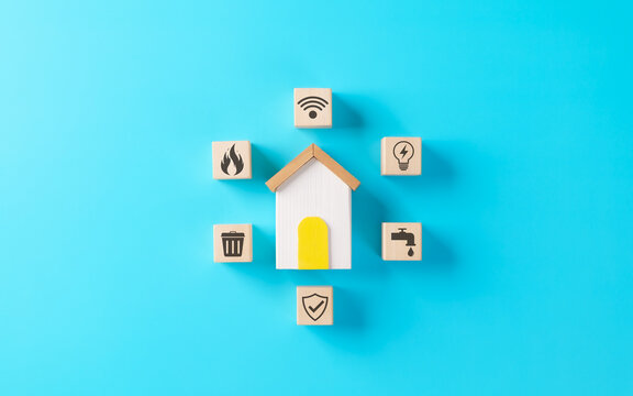 Home Utilities and Services Concept. Wooden blocks with icons for utilities like water, electricity, internet, gas, waste, and insurance are arranged around model house symbolizing household services.