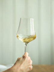 hand swirling a glass of white wine against white wooden wall