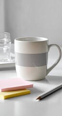 A gray-striped mug sits on a white surface, beside sticky notes and a pencil