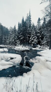 Vertical view of a snow-covered creek flowing into a partially frozen waterfall in Algonquin Park