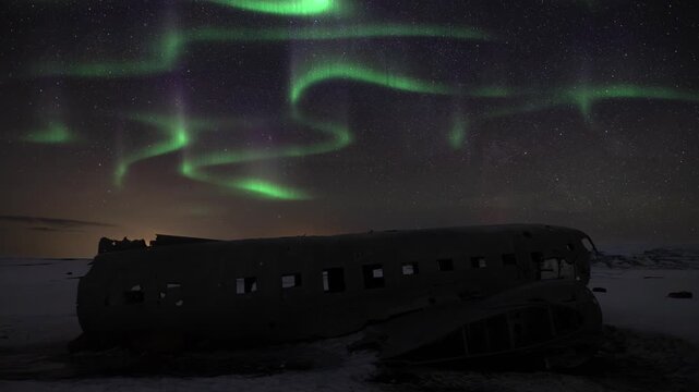 Time lapse of Aurora borealis above a crashed DC-3 Plane in Solheimasandur Iceland during winter. Tourism landmark at night with stars and sky.