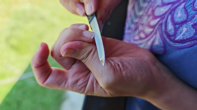 Professional manicurist filing fingernails using metallic tool, demonstrating meticulous beauty care and precise nail shaping technique
