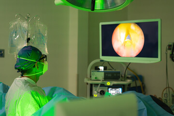 Doctor in surgical gown and mask performing a urological laser procedure while observing the...