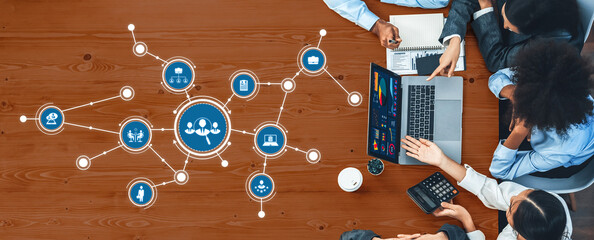 A diverse team engages in a collaborative meeting over a wooden table, utilizing digital tools and visual aids to discuss innovative strategies and data insights. Amity