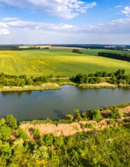 Fototapeta premium High-angle view of a river winding through agricultural fields, lush greenery, and a partly cloudy sky