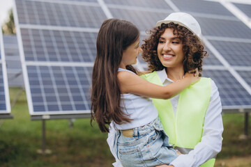 Engineer holding her daughter smiling in front of solar panels