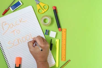 Hand writing back to school message on notebook with colorful school supplies on green background, preparing for new academic year