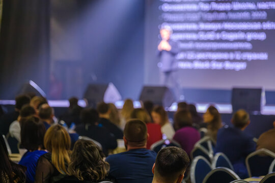 Large audience attending a presentation at a business event with focus on speaker on stage.