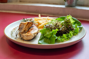 Close-up of grilled chicken breast garnished with rosemary, served with french fries and fresh salad, showcasing a delicious and healthy meal