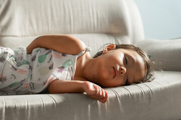 Little girl sleeping on a light gray sofa, afternoon light, arm relaxed over the edge, peaceful nap at home.