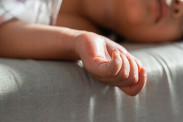 Macro detail of a child&rsquo;s hand hanging off couch edge, shallow depth of field, calm indoor nap mood