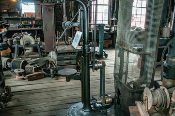 A historic workshop showcases vintage machinery, hand tools, and old equipment scattered across wooden floors, highlighting the charm of craftsmanship in a rustic environment.