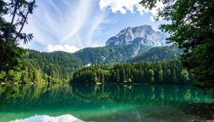 Naklejka premium Serene mountain lake nestled amongst lush forests, reflecting a majestic peak under a vibrant blue sky.