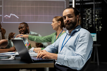 Male accounting manager reviewing budget numbers after all monthly costs, reviewing data updates on laptop during night time meeting with his work team. After hours night scene.