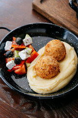 Mashed potatoes with crispy cutlets and fresh Greek salad on a black rustic plate
