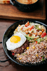 Healthy lunch bowl with buckwheat, beef patty, sunny-side egg and fresh Caesar salad
