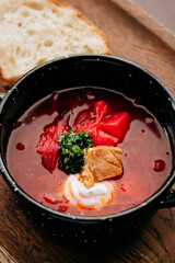 Traditional Ukrainian borscht with sour cream, pork, and fresh herbs in a black rustic bowl