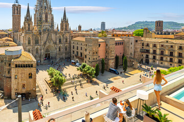Tourists and young people at a rooftop bar with swimming pool overlooking the plaza and Gothic...