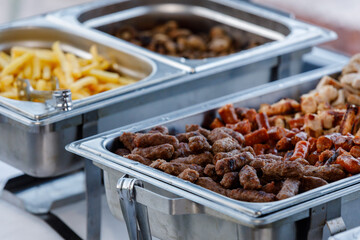 Delicious buffet selection featuring grilled meats and french fries at an outdoor gathering in the afternoon sun