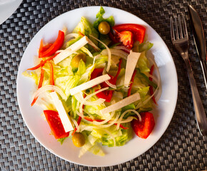 Plate of colorful appetizing salad of fresh greens, slices of tomato and onion, marinated olives and soft cheese. Healthy appetizer concept