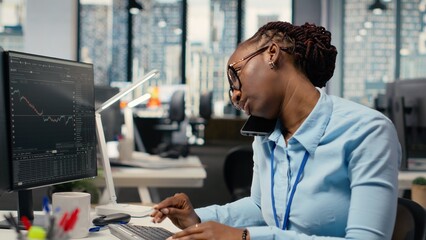 Equity analyst in office reviews quarterly earnings paperwork to assess future stock market value, talking on phone. Trader making calls, conducting financial analysis to improve investments