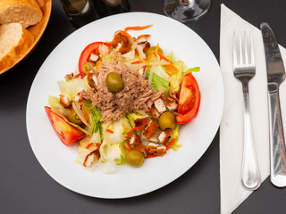 Salad of fresh vegetables, pickled olives and meat is prepared on plate. Dish is served warm with glass of dry red wine