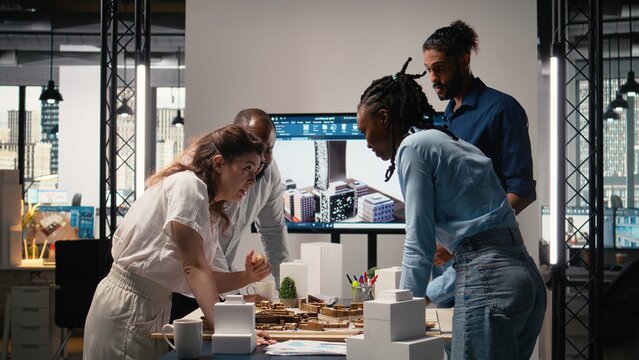 Close up of developers arranging 3D models to explore residential layout options, working on structural city planning for urban development project during a strategic team meeting.