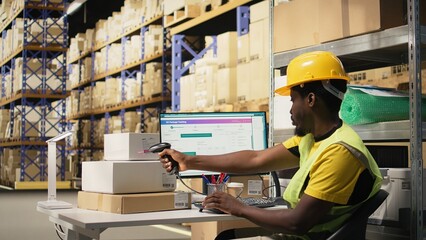 Black staff member using a barcode scanner to process shipping labels on boxes from industrial storage racks. Scanning awb tags for package tracking service and accurate logistics. Camera A.